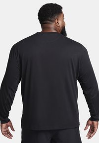 Black long-sleeve shirt with a round neckline, smooth fabric, and flat seams. Features a relaxed fit and a slightly curved hem at the back.