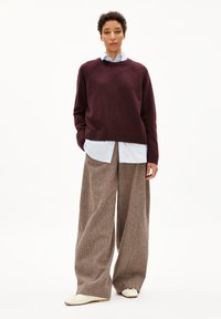 Bordeauxfarbener Strickpullover mit Rundhalsausschnitt über einem hellblauen Hemd mit Kragen, kombiniert mit weiten beige strukturierten Hosen und cremefarbenen Schuhen.