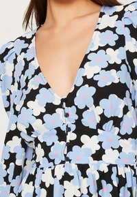 Blomklänning med svart bakgrund som har ljusblå och rosa blommor, en djup V-ringning, puffärmar och svarta knappar framtill.