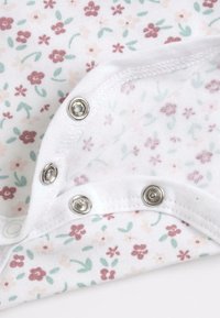 Cache-cœur en coton blanc avec petit imprimé floral rose et vert, doté de boutons-pression argentés au bas pour un habillage facile.