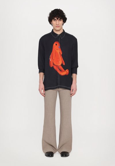 Button-up shirt in black fabric, featuring an orange cartoon dog design on the front. Paired with beige flared trousers and black shoes.