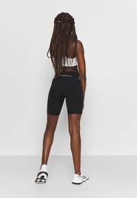 Czarne sportowe szorty o slim fit i średniej wysokości w pasie, w zestawieniu z białą krótką bluzką na ramionkach i białymi sneakersami. Prosty design bez wzorów.