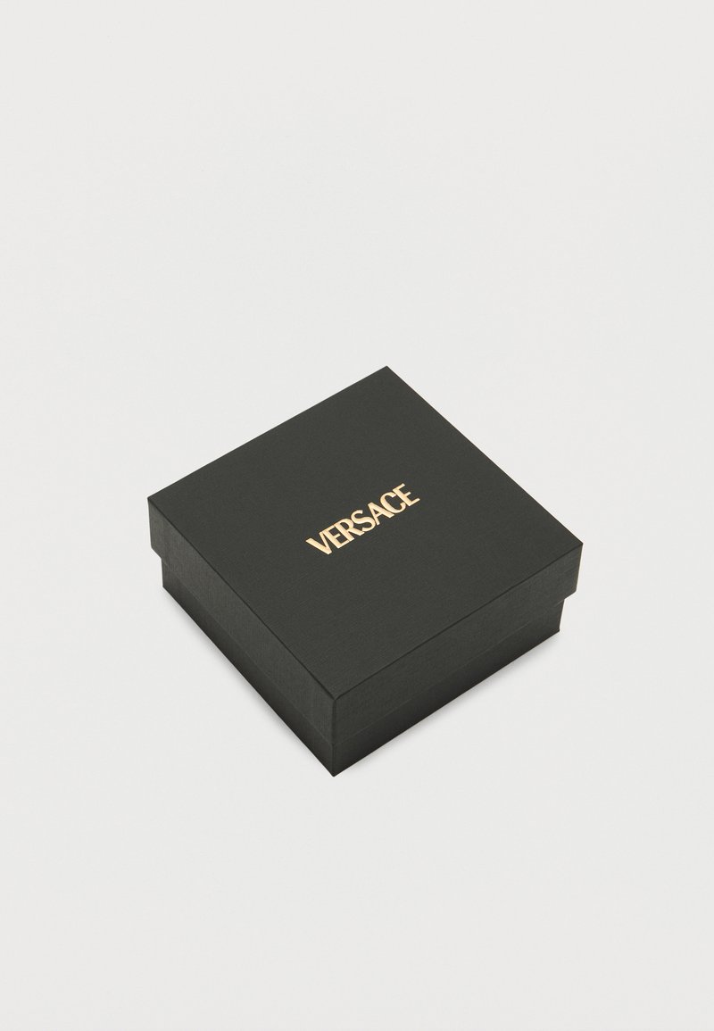 Schwarze strukturierte Box mit quadratischer Form, die oben ein goldenes "VERSACE"-Logo zeigt. Das Design ist minimalistisch und elegant.