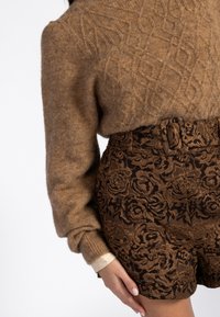 Bruine wollen trui met getextureerde diamanten patronen, gecombineerd met hoog-getailleerde shorts met een bloemenpatroon in donkerbruin en gouden accenten.