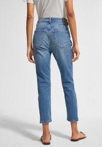 Vaqueros de mezclilla azul claro con corte recto, que cuentan con dos bolsillos traseros y un dobladillo ligeramente deshilachado. Detalles de cinturón y etiqueta de cuero.