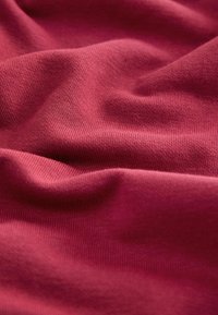 Südamlik puuvillane kangas, millel on sile tekstuur ja peen kudumismuster, näidates õrnu voltisid ja langusi, mis viitavad pehmusele ja paindlikkusele.