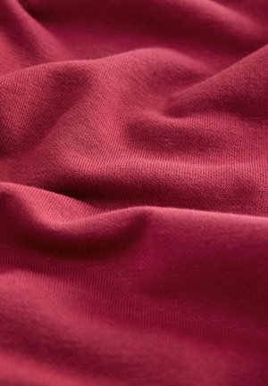 Veripunaisesta puuvillakankaasta, jossa on sileä pinta ja hieno neulomiskuvio, näkyy lempeitä laskoksia ja laskostuksia, jotka viittaavat pehmeyteen ja joustavuuteen.