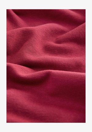 Karmozijnrode katoenen stof met een gladde textuur en fijn breipatroon, met zachte plooien en vallen, wat zachtheid en flexibiliteit aangeeft.