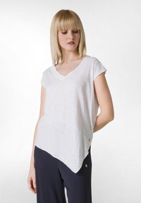 Top alb cu mânecă scurtă, decolteu în V, cu o croială lejeră și tiv asimetric. Fabricat dintr-un material ușor, cu textură.