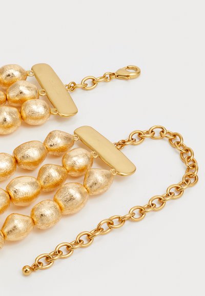 Goldfarbene Halskette mit strukturierten runden Perlen, flachen rechteckigen Elementen und einer verbundenen Kette. Das Design ist geschichtet mit unterschiedlichen Perlenformen.