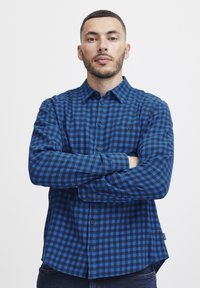Mėlynos ir juodos languotos marškiniai, pagaminti iš flanelės; turi užsegimą priekyje, apykaklę ir krūtinės kišenę; įprasto kirpimo, ilgos rankovės.