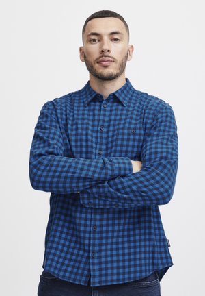 Camisa a cuadros azul y negra hecha de tela de franela; cuenta con un cierre frontal de botones, cuello y un bolsillo en el pecho; corte regular con mangas largas.