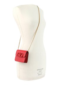 Bolso cruzado de cuero rojo con correa de cadena dorada exhibido en un maniquí blanco.