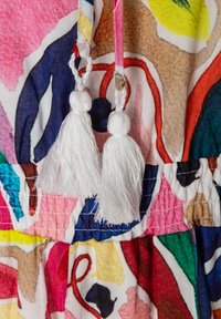 Bunte Stoffe mit abstrakten Mustern in Pink, Blau und Gelb, mit weißen Quasten und einem gerafften Taillendetail.