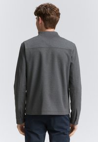 Szara bluza z wysokim kołnierzem i długimi rękawami. Gładka, teksturowana tkanina. Prosty design z prostym krojem i minimalnymi szwami.