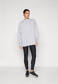 Sudadera gris de gran tamaño con un alto cuello, combinada con leggings negros con un logo y zapatillas deportivas negras. Un look simple y deportivo.