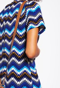 Vestido de manga corta con un patrón geométrico en azul, marino, blanco y marrón. Incluye una tira marr�ón que cruza el hombro.