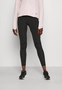 Schwarze Sportleggings aus glattem Stoff, figurbetontes Design, kombiniert mit einer hellrosa Langarm-Zip-Jacke und schwarzen Turnschuhen.
