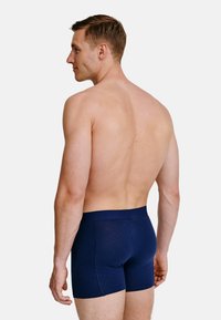 Námořnické modré bavlněné boxerky s přiléhavým střihem, měkkou texturou a širokým pasem, zobrazené zezadu na holém trupu.