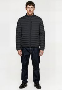 Black puffer jacket with horizontal quilted design, high collar, front zipper, paired with dark denim jeans and black shoes.