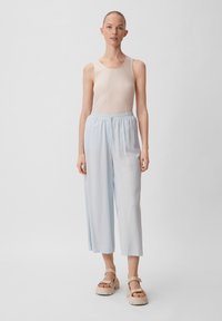 Pantaloni larghi azzurri con vita elastica, abbinati a una canotta a coste color crema. Il modello si trova su uno sfondo neutro, indossando sandali con plateau beige.