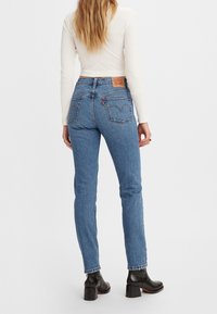 Jeans blu con vita alta e vestibilità slim, caratterizzati da un design distintivo della tasca posteriore e da un'etichetta in pelle. Stivaletti neri completano il look.