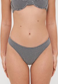 Bas de bikini à carreaux noir et blanc avec une taille basse et une texture lisse, présentant un design simple et sans matériel visible.
