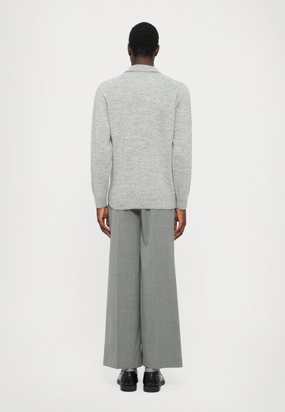 Suéter gris de punto con mangas largas, que presenta un dobladillo acanalado. Combinado con pantalones anchos gris y zapatos negros, visto desde atrás.
