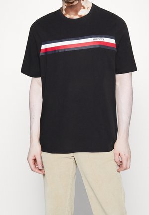 T-shirt en coton noir avec un design à rayures horizontales rouges, blanches et bleues sur la poitrine, avec un texte de logo sur la bande.