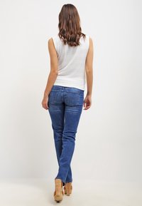 Witte mouwloze top, blauwe skinny jeans en beige high heels. Glad materiaal, getailleerd ontwerp met subtiele details op de top.