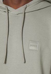 Sudadera con capucha de color gris claro con un parche texturizado del logo BOSS en el pecho. Cuenta con cordones con puntas de plástico y puños acanalados. Tejido suave.