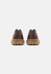 Brown leather shoes with a textured finish, featuring a chunky, light tan rubber sole and visible stitching along the edge.