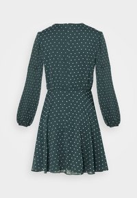 Robe longue à manches longues vert foncé avec de petits motifs de cœurs blancs, taille ajustée et jupe évasée, vue de dos sur un fond uni.