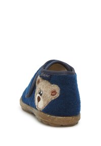 Niebieskie wełniane kapcie z brązową twarzą misia po boku, elastycznym paskiem, textured (teksturalną) podeszwą i zaokrąglonym kształtem. Miękki materiał zwiększa komfort.