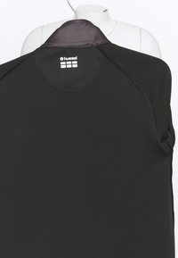 T-shirt de sport noir à manches longues avec col rayé, logo "hummel" et étiquette de taille à l'intérieur de l'encolure arrière.