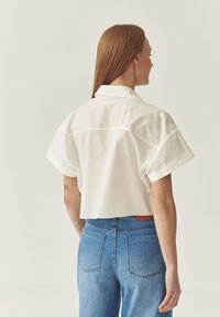 Cropped white shirt with short sleeves and a pointed collar, paired with high-waisted blue jeans featuring a back pocket design.