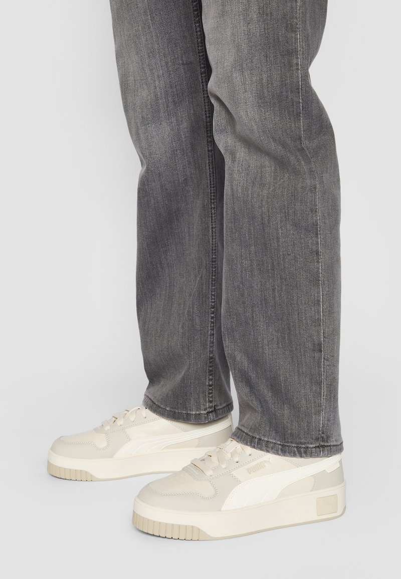 Baskets beiges avec une tige texturée, des accents blancs et une semelle épaisse. Associées à un pantalon en denim gris à coupe droite.