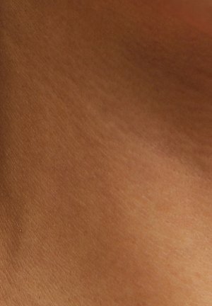 Peau brune lisse et uniformément teintée, avec des pores naturels visibles et de fines ridules sous un éclairage doux.