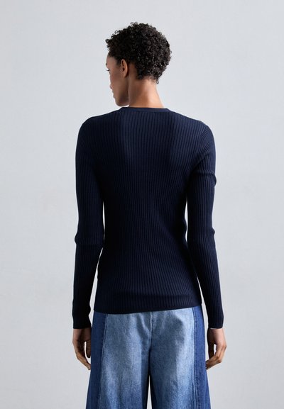 Marineblauer, gerippten Langarmpullover mit taillierter Passform, Rundhalsausschnitt und glatter Textur, kombiniert mit weiten hellblauen Jeanshosen.