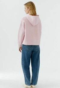 Sweat-shirt à capuche rose de coupe décontractée avec poignets côtelés, associé à un jean denim bleu taille haute avec poches arrière et coupe droite.