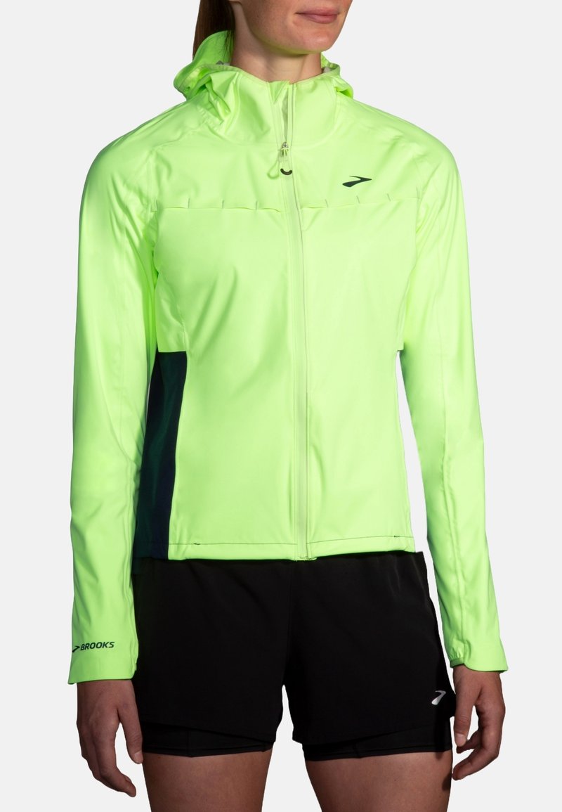 Veste de course à haute visibilité de couleur vert néon, dotée d'une capuche, d'une fermeture éclair et de panneaux latéraux de couleur foncée. Tissu léger et respirant, idéal pour une utilisation active.