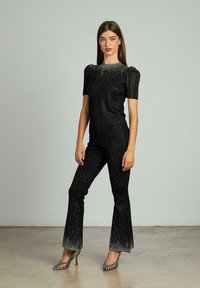 Conjunto negro de dos piezas con mangas cortas y abullonadas y pantalones acampanados, que presenta acentos metálicos y adornos en degradé en el dobladillo.