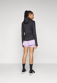 Haut de sport noir à manches longues avec capuche, associé à un short violet clair, des chaussettes noires et des baskets noires avec des accents blancs.
