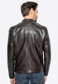 Giacca di pelle marrone con una texture liscia, design aderente e delicati dettagli sulle spalle, vista da dietro. Presenta una cucitura classica.