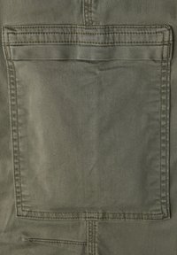 Olivengroen stof heeft een grote achterzak met gestikte randen, en toont een gladde textuur en een subtiele glans.