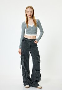 Grauer langärmliger Crop-Top mit V-Ausschnitt und weißem Unterlayer, kombiniert mit hoch taillierten schwarzen Cargo-Hosen mit mehreren Taschen und lockerer Passform.