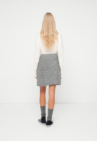 Gonna grigia a maglia con una superficie texture, abbinata a sneaker nere e calzini grigi a coste. Lo sfondo è bianco semplice.