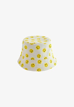 Chapeau seau blanc doté d'un motif répété d'emojis de visages souriants jaunes. Fait en tissu avec une texture douce et un large bord.