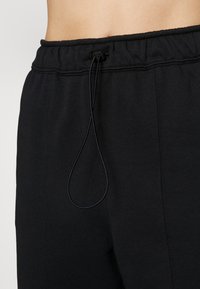 I pantaloni sportivi neri presentano un elastico in vita con cordino, una texture liscia e cuciture lungo le gambe.