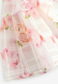 Kukkakuosiset mekko, jossa on läpinäkyvä, kevyt kangas pehmeissä vaaleanpunaisissa ja vihreissä väreissä. Huomiota herättävinä yksityiskohtina on hennot rypytykset.